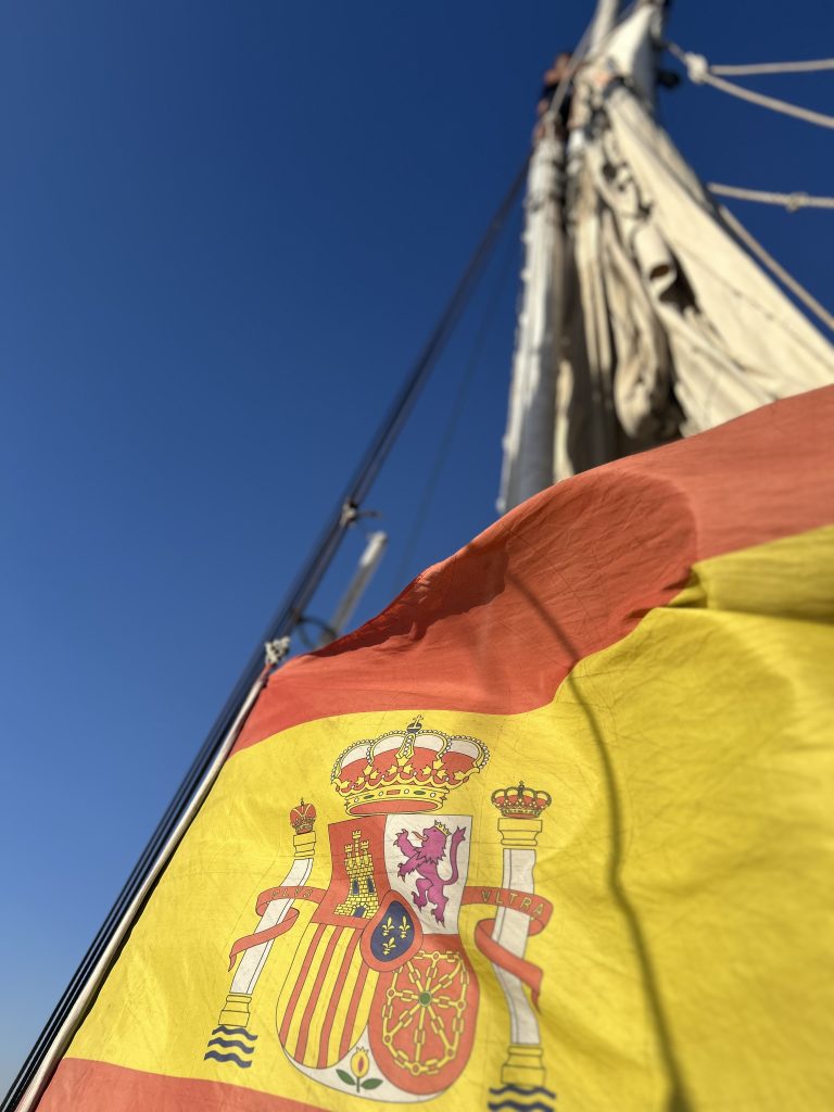 La bandera española ondeando en una felucca, símbolo del poder observado desde el movimiento y la distancia