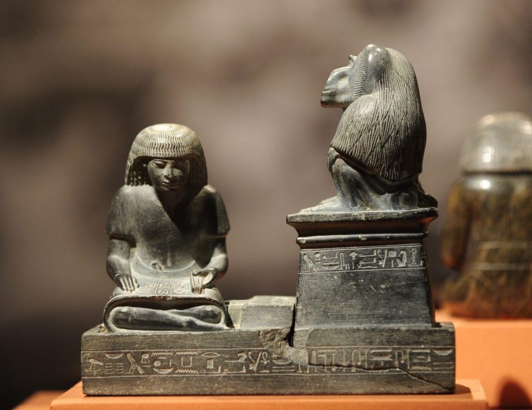 Escultura egipcia de un escriba sentado con rollo de papiro junto a una divinidad, símbolo del poder del conocimiento y del monopolio de la escritura en el Antiguo Egipto.